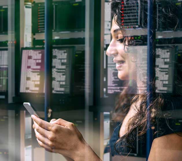 Engineer checking a phone in front of server racks reflected in glass