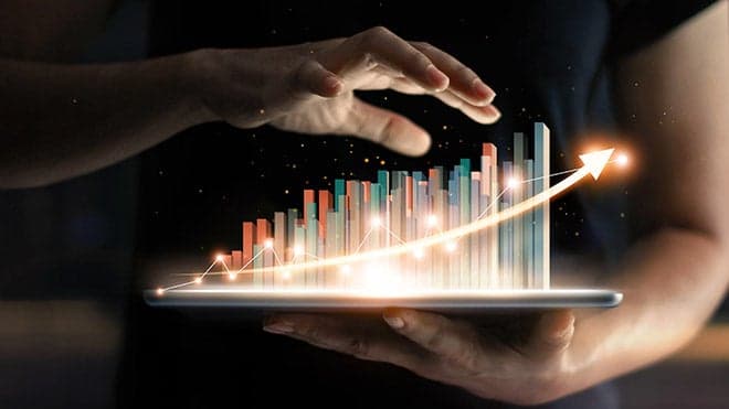 Hands holding a tablet projecting a rising holographic bar chart, growth in the cloud
