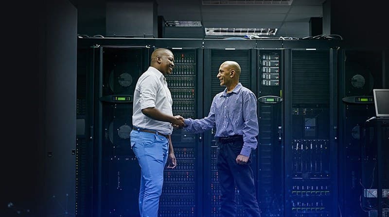 Two IT staff shaking hands between server racks in a data centre